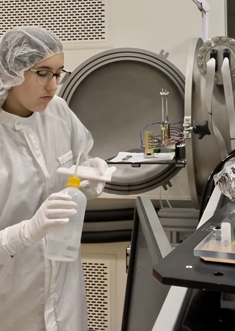 Waldych, wearing a special gown, hairnet and gloves, is applying isopropyl alcohol to a cloth that will be used to clean all the equipment before an experiment. All the experimental work is performed in a clean room to prevent extra dust or oils from contaminating a very sensitive thermal experiment inside the vacuum chamber. 